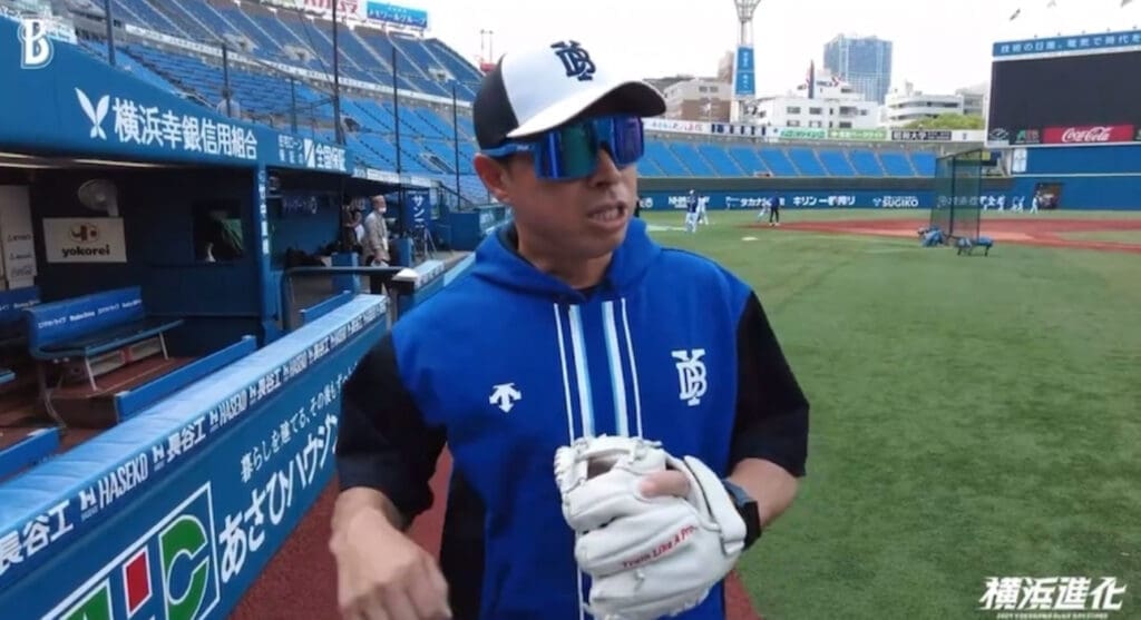 Coach Hiroyasu Tanaka at Yokohama DeNA baseball field, adjusting equipment.